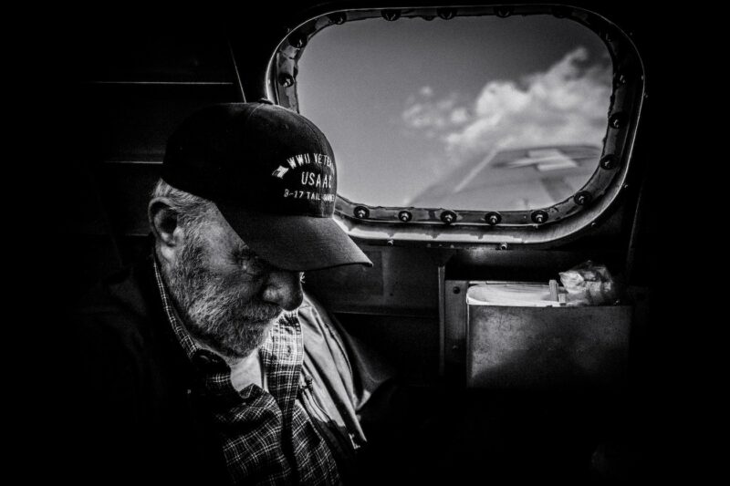 World War II Veteran and B-17 Tailgunner looking out of the window of a preserved bomber in flight, symbolizing Carmen's mission to Let Me Guide You Home.